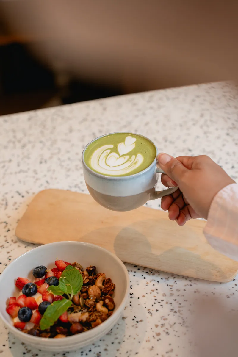 Matcha latte beside a fruit and granola bowl